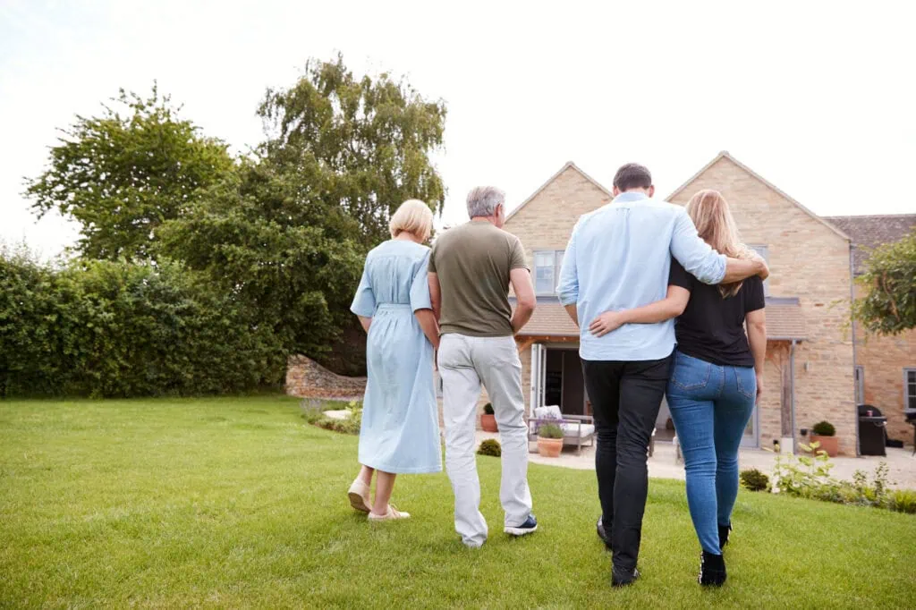 rear view of family with senior parents and adult offspring walking and talking in garden together