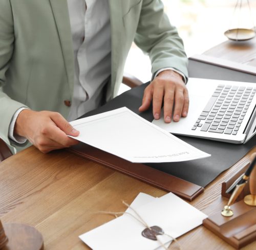 Male notary with documents and laptop at table in office, closeup